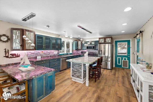 kitchen with appliances with stainless steel finishes, hanging light fixtures, light hardwood / wood-style floors, a barn door, and dark stone counters