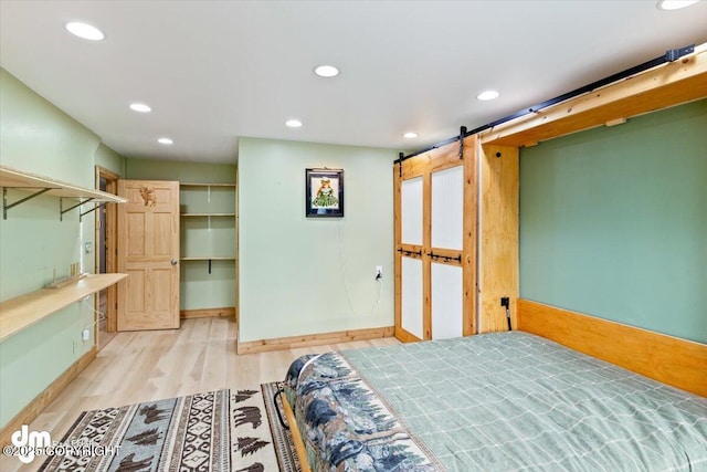 bedroom with a walk in closet, a barn door, and light hardwood / wood-style flooring