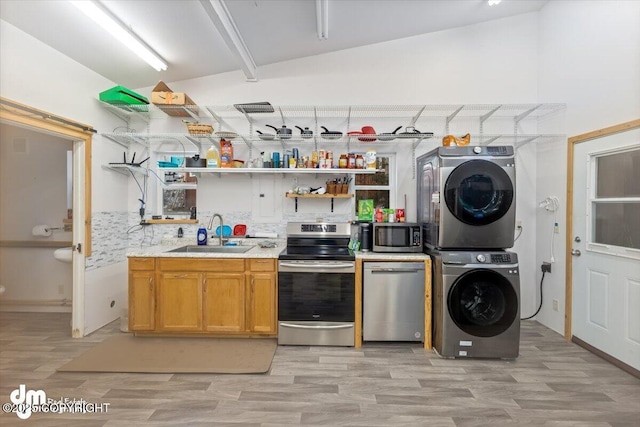 kitchen featuring stainless steel appliances, sink, stacked washer / drying machine, and light hardwood / wood-style flooring