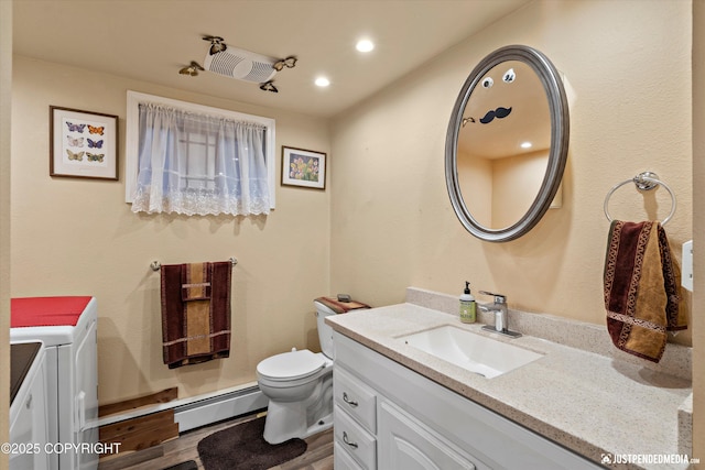 bathroom with a baseboard radiator, washer / dryer, wood-type flooring, vanity, and toilet