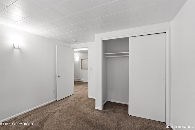 unfurnished bedroom featuring a baseboard radiator, dark carpet, and a closet