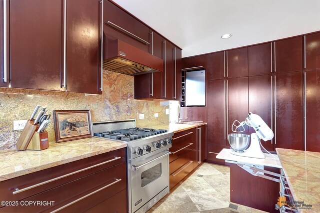 kitchen with extractor fan, light stone countertops, luxury stove, and decorative backsplash