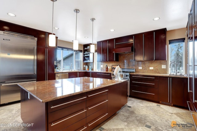 kitchen with hanging light fixtures, plenty of natural light, a kitchen island, stainless steel appliances, and decorative backsplash