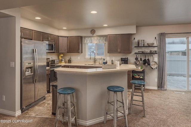 kitchen with sink, stainless steel appliances, a kitchen breakfast bar, dark brown cabinetry, and a kitchen island