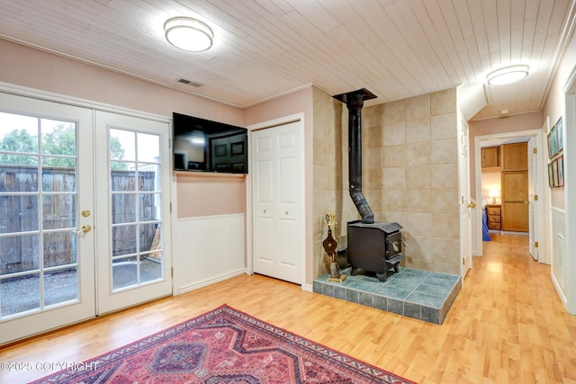 living room featuring wood ceiling, wood-type flooring, ornamental molding, french doors, and a wood stove