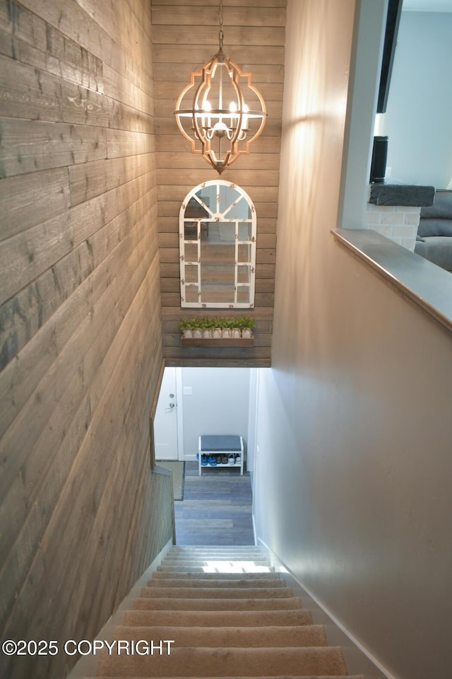 stairway featuring an inviting chandelier and wood walls