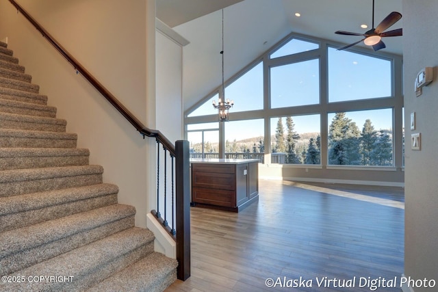 stairs with wood-type flooring, a mountain view, ceiling fan with notable chandelier, and high vaulted ceiling