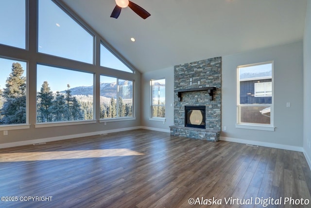 unfurnished living room featuring ceiling fan, high vaulted ceiling, dark hardwood / wood-style flooring, a mountain view, and a stone fireplace