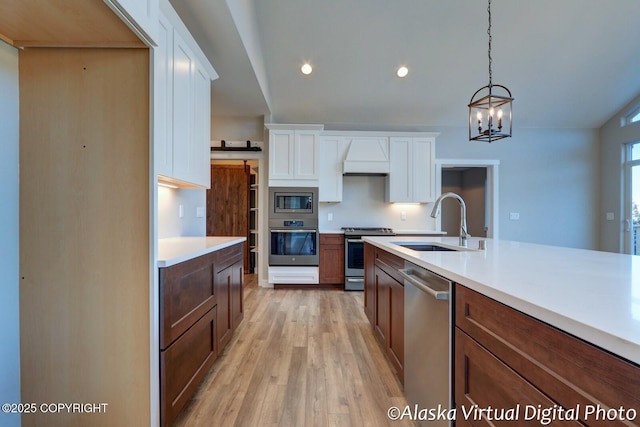 kitchen featuring sink, light hardwood / wood-style flooring, white cabinetry, stainless steel appliances, and decorative light fixtures