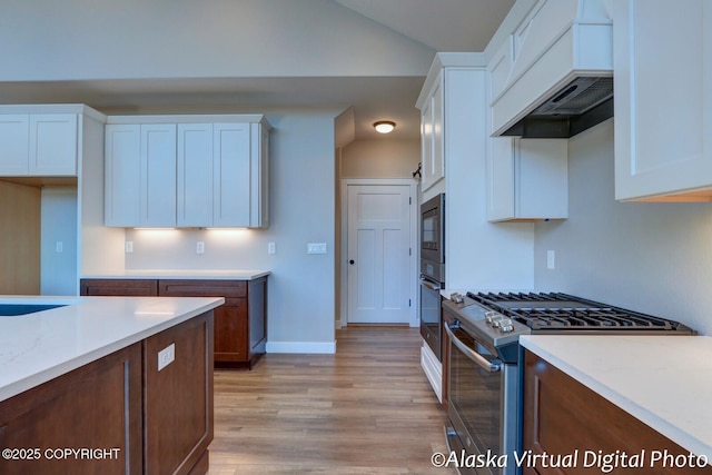 kitchen featuring vaulted ceiling, stainless steel range with gas stovetop, white cabinets, custom exhaust hood, and light wood-type flooring