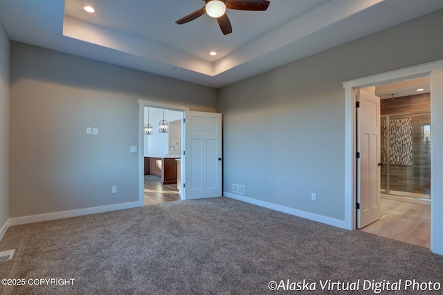 unfurnished bedroom featuring sink, light carpet, ensuite bath, and a tray ceiling