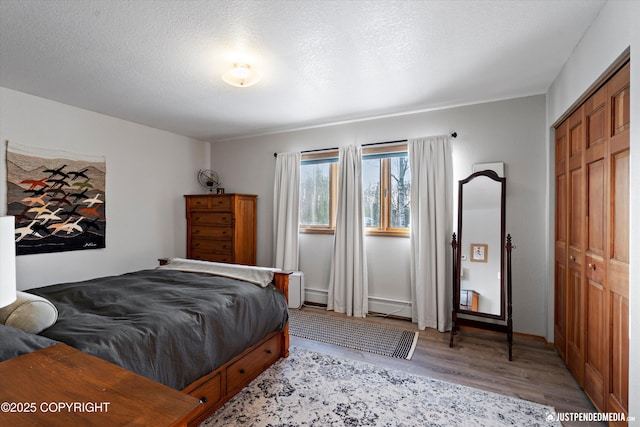 bedroom with light hardwood / wood-style floors, a closet, a textured ceiling, and baseboard heating