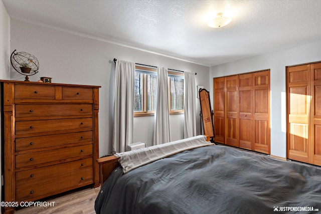 bedroom featuring two closets, a textured ceiling, and light hardwood / wood-style flooring