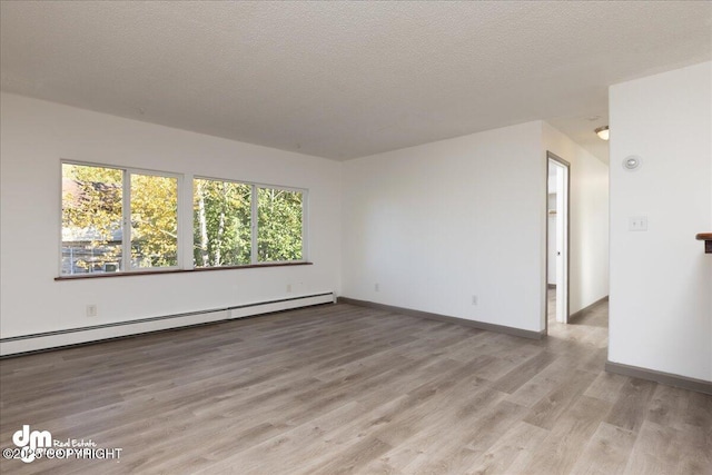 empty room featuring a textured ceiling, baseboard heating, light wood-type flooring, and baseboards