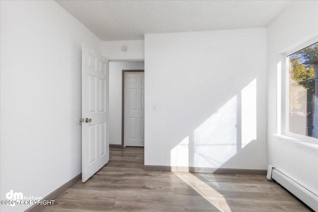 empty room with a baseboard heating unit, light wood finished floors, a textured ceiling, and baseboards