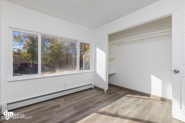 unfurnished bedroom featuring baseboard heating, wood finished floors, and baseboards