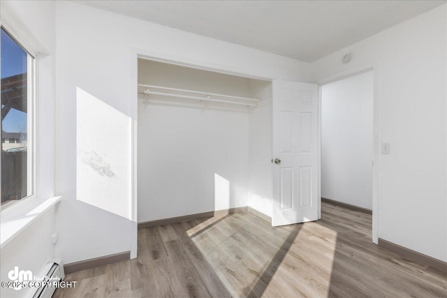 unfurnished bedroom featuring a baseboard heating unit, a closet, wood finished floors, and baseboards