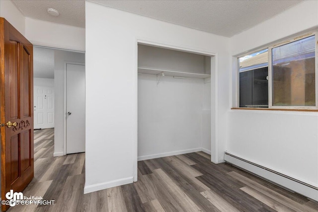 unfurnished bedroom featuring a textured ceiling, a closet, baseboard heating, and dark wood finished floors