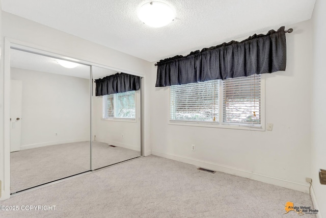 unfurnished bedroom with a closet, visible vents, light colored carpet, a textured ceiling, and baseboards