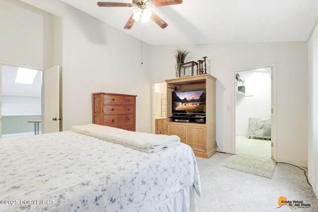 bedroom featuring ceiling fan, vaulted ceiling with skylight, light colored carpet, baseboards, and a spacious closet