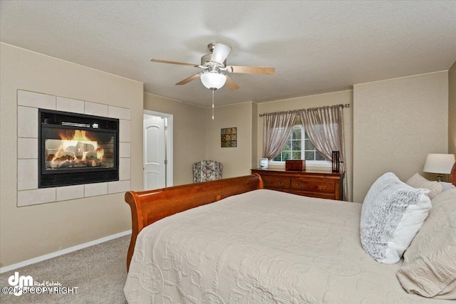 bedroom with a tiled fireplace, light carpet, a textured ceiling, and ceiling fan