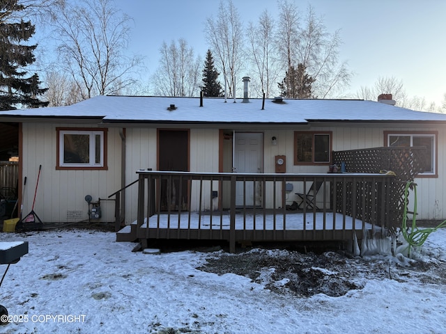 snow covered back of property with a deck