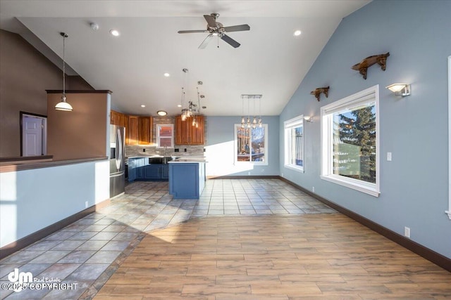 kitchen featuring stainless steel fridge, hanging light fixtures, backsplash, a kitchen island, and ceiling fan with notable chandelier