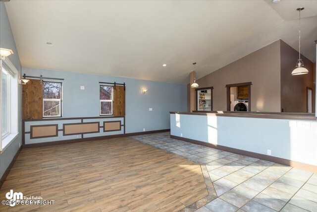 unfurnished living room with high vaulted ceiling, washer / dryer, light hardwood / wood-style floors, and a barn door