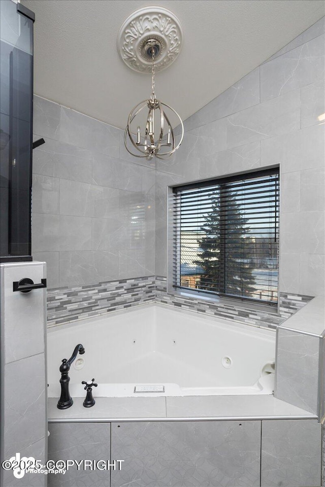 bathroom featuring tiled bath and a chandelier