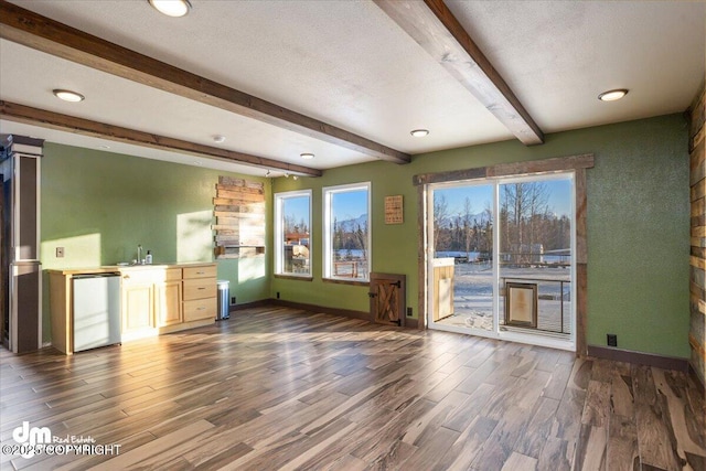 unfurnished living room with dark wood-type flooring, sink, a textured ceiling, and beamed ceiling