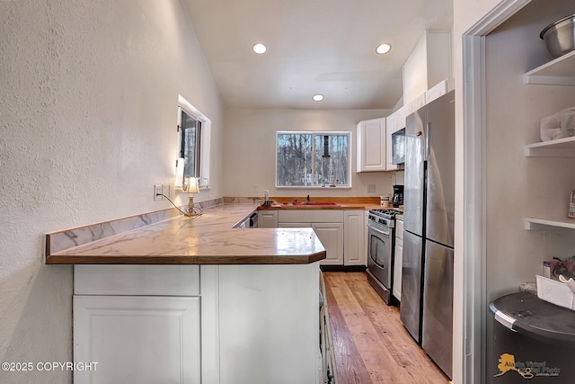 kitchen featuring sink, white cabinets, kitchen peninsula, stainless steel appliances, and light hardwood / wood-style flooring