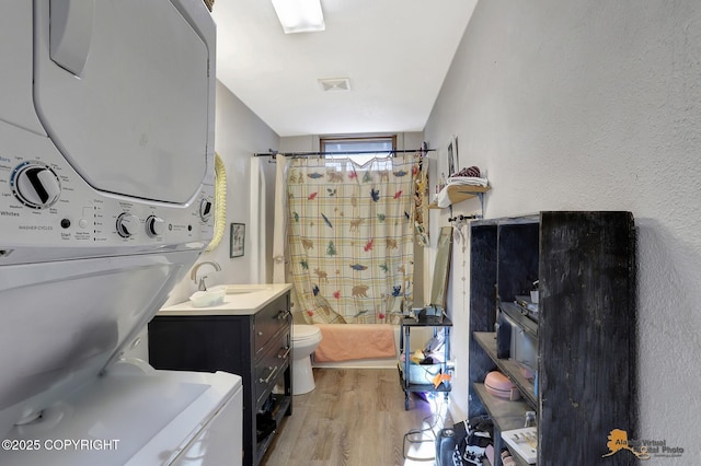 bathroom with hardwood / wood-style flooring, stacked washer and dryer, vanity, and toilet