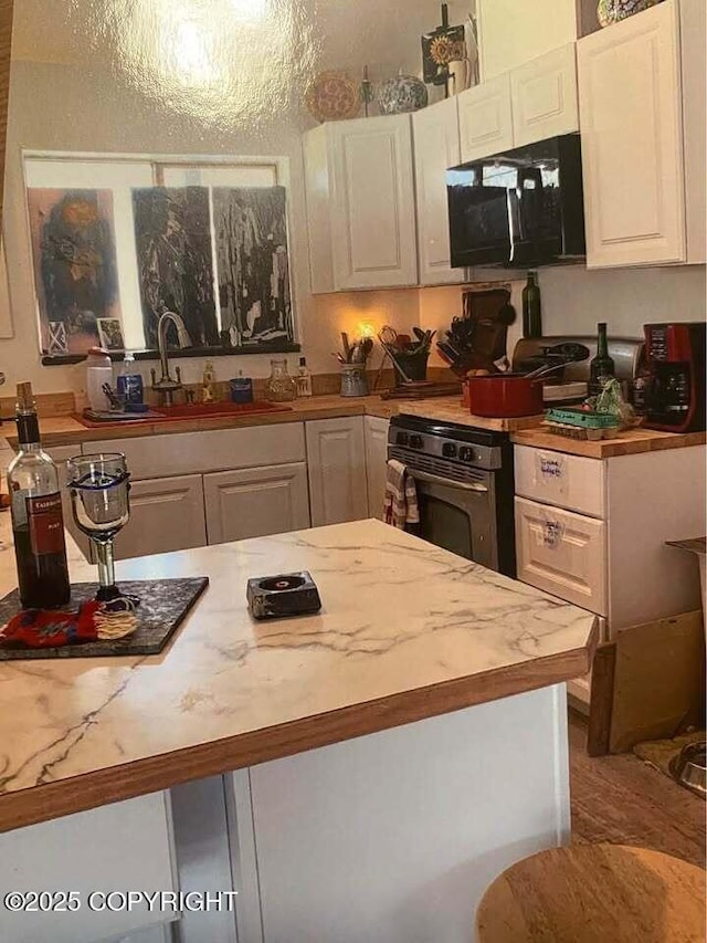 kitchen featuring white cabinetry, sink, stainless steel stove, and light stone counters