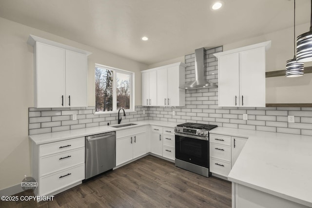 kitchen with pendant lighting, white cabinetry, sink, stainless steel appliances, and wall chimney exhaust hood