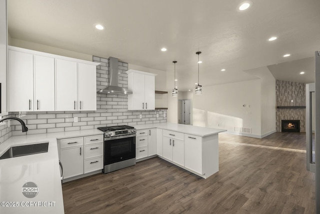 kitchen featuring wall chimney range hood, sink, stainless steel gas stove, hanging light fixtures, and kitchen peninsula