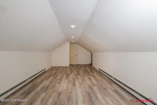 bonus room featuring light wood-type flooring, vaulted ceiling, a textured ceiling, and a baseboard heating unit