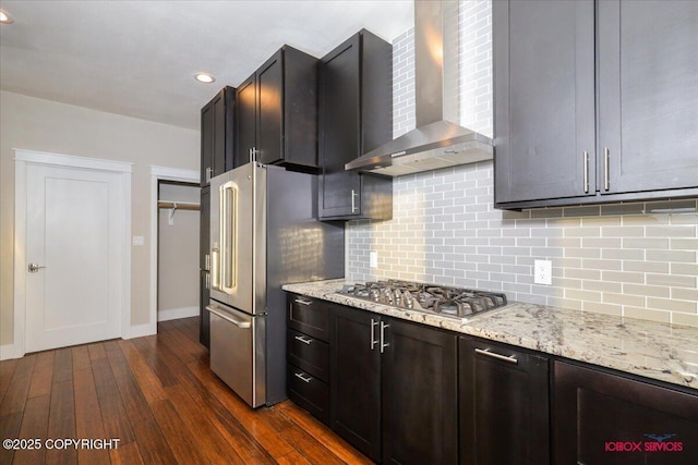 kitchen featuring tasteful backsplash, light stone counters, stainless steel appliances, dark wood-type flooring, and wall chimney exhaust hood