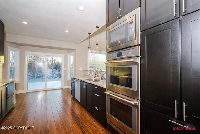 kitchen featuring light stone counters, stainless steel appliances, decorative light fixtures, and sink