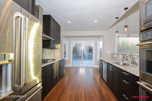 kitchen with sink, hanging light fixtures, dark hardwood / wood-style floors, stainless steel appliances, and light stone countertops