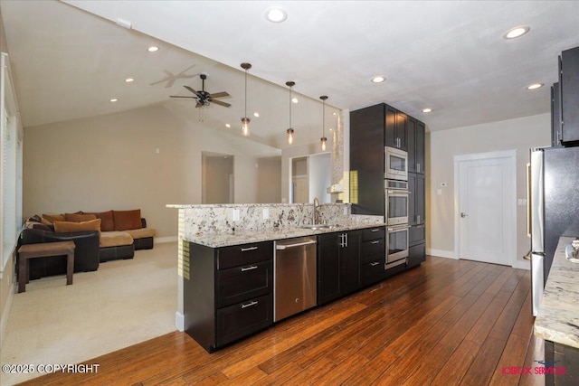 kitchen featuring lofted ceiling, hanging light fixtures, kitchen peninsula, stainless steel appliances, and light stone countertops