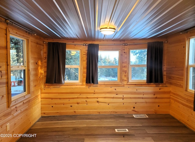 spare room with hardwood / wood-style floors, wooden walls, and a healthy amount of sunlight