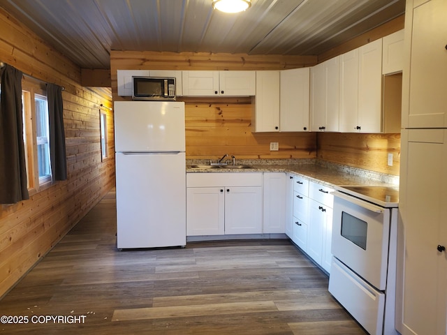 kitchen with white cabinetry, sink, white appliances, and wood walls