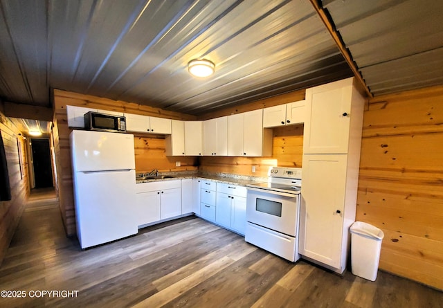 kitchen with wooden walls, sink, white cabinets, dark hardwood / wood-style flooring, and white appliances