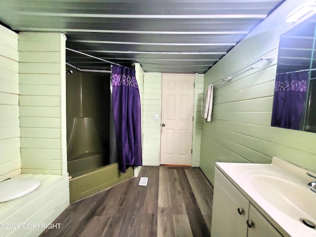 bathroom with shower / bath combo, wood-type flooring, vanity, and wooden walls