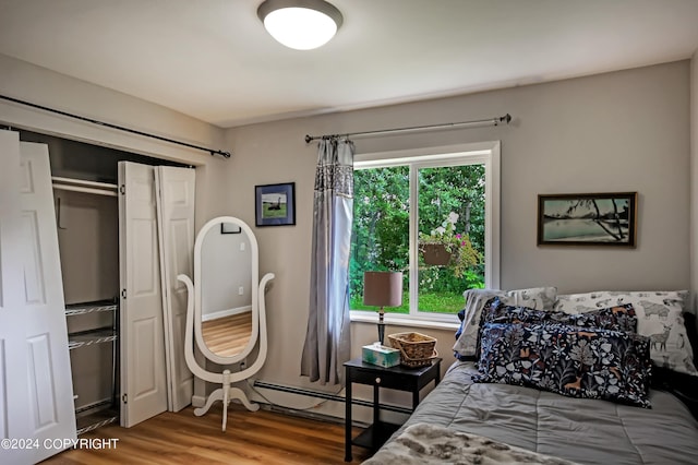 bedroom featuring a baseboard heating unit, a closet, and wood-type flooring