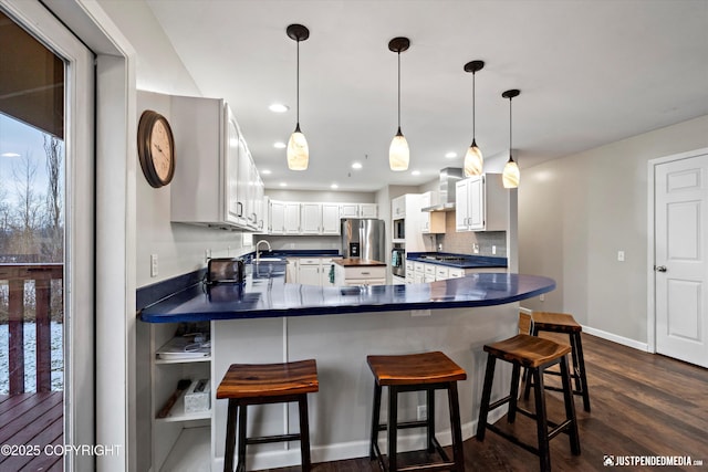 kitchen with wall chimney range hood, a breakfast bar, stainless steel fridge, sink, and white cabinetry