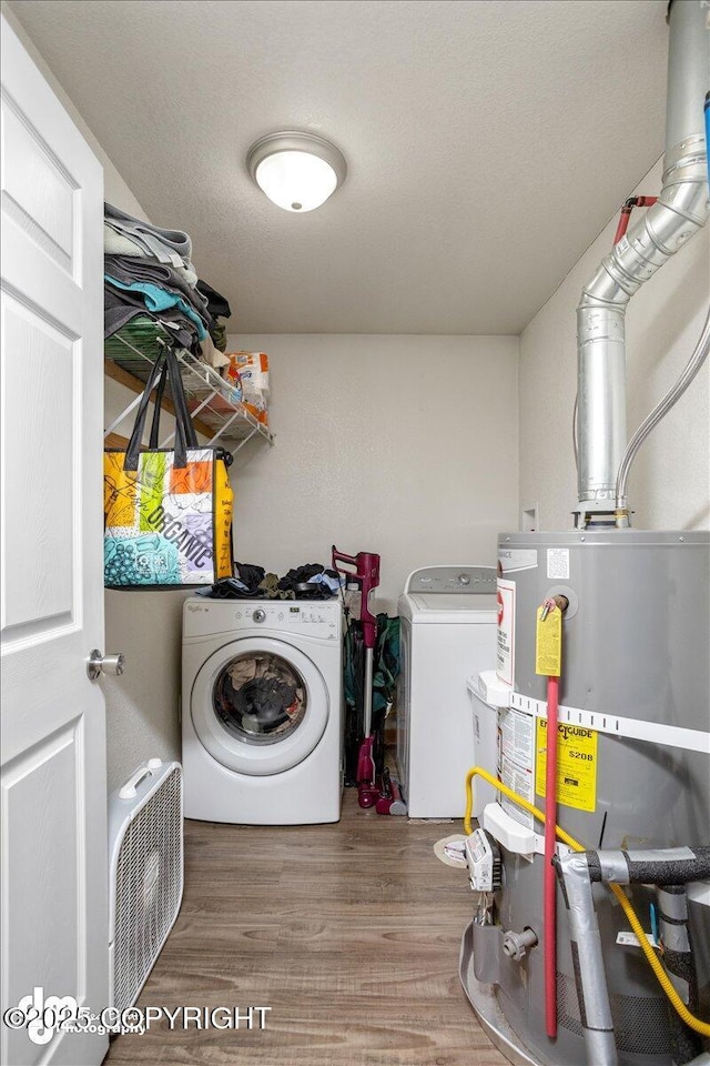 clothes washing area with water heater, wood-type flooring, and washer and dryer