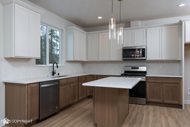 kitchen with white cabinetry, hanging light fixtures, appliances with stainless steel finishes, a kitchen island, and light hardwood / wood-style floors