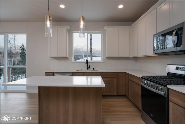 kitchen featuring sink, appliances with stainless steel finishes, a kitchen island, pendant lighting, and white cabinets