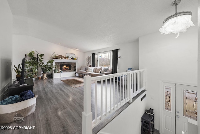 living area featuring lofted ceiling, a stone fireplace, wood finished floors, and a textured ceiling